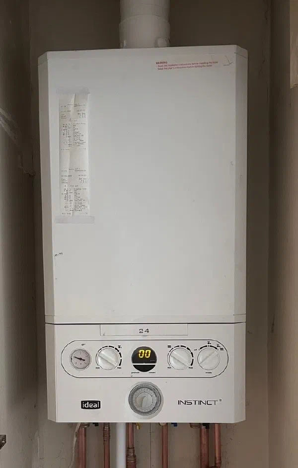 Ideal Instinct 2 combi boiler fitted in an alcove, with the commissioning printout taped to the casing and copper pipework beneath