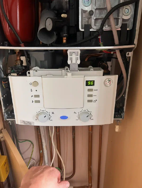 Boiler opened up for servicing, showing the expansion vessel, gas valve and internal wiring behind the control panel